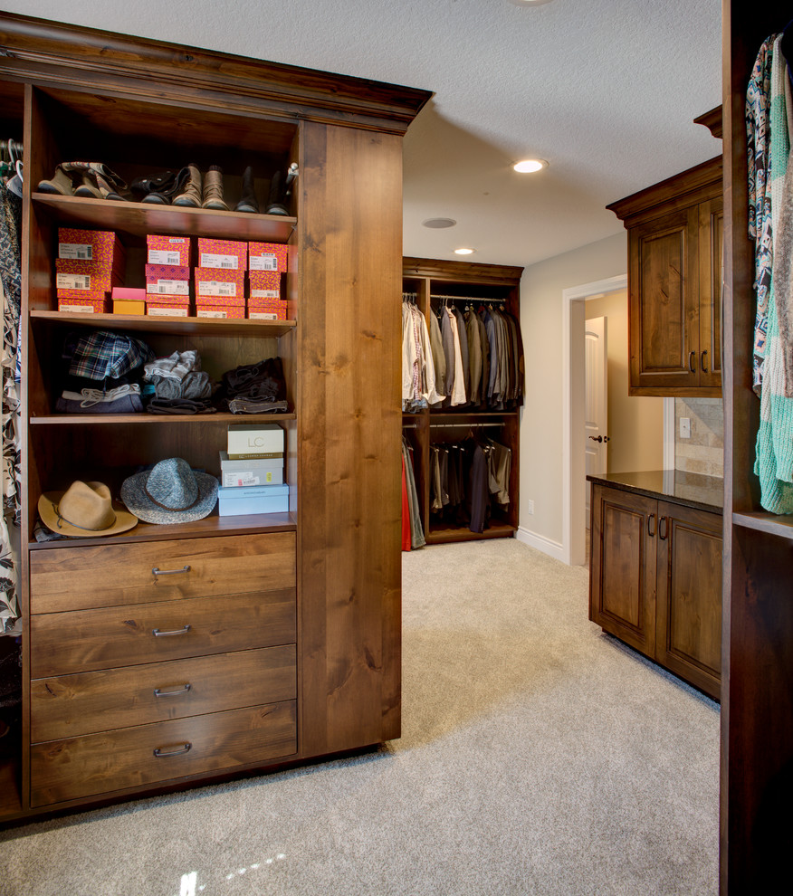 Large country gender-neutral walk-in wardrobe in Kansas City with raised-panel cabinets, medium wood cabinets and carpet.