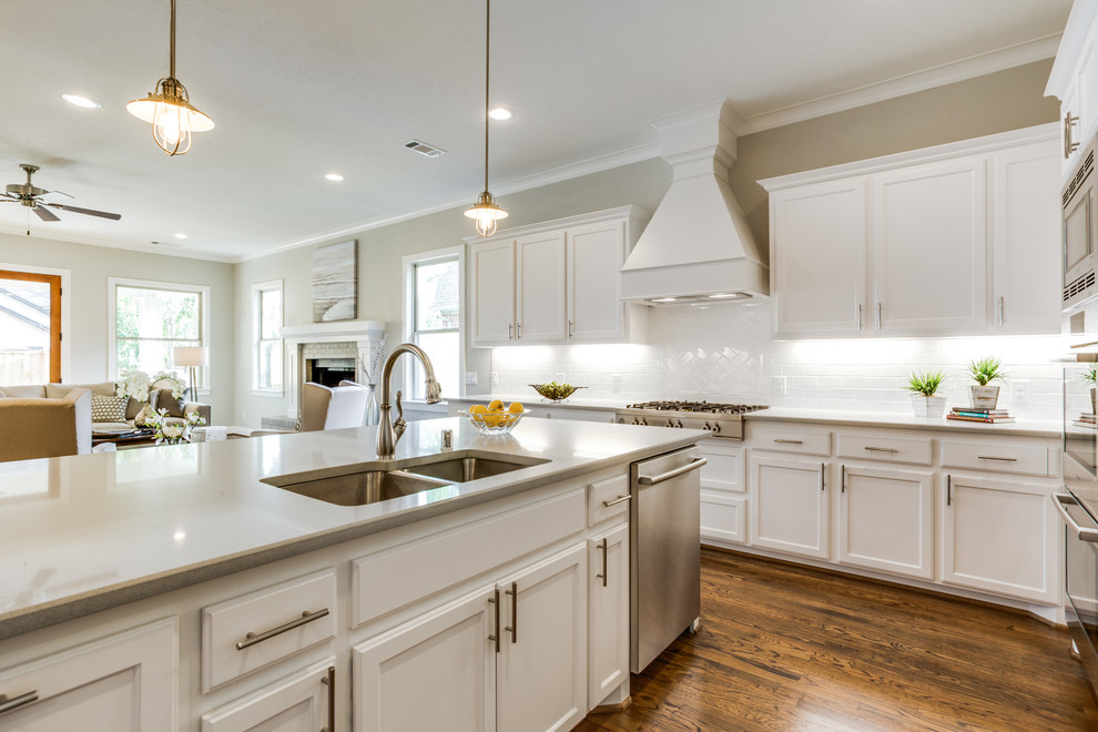 This is an example of a mid-sized traditional l-shaped open plan kitchen in Dallas with an undermount sink, shaker cabinets, white cabinets, quartz benchtops, white splashback, ceramic splashback, stainless steel appliances, medium hardwood floors and with island.