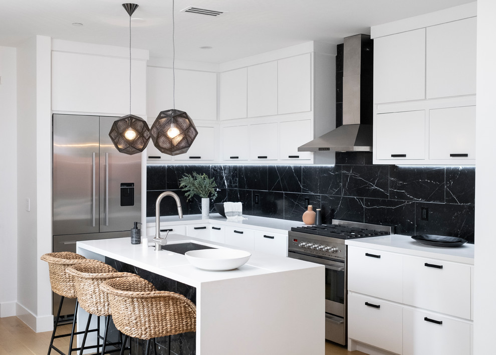 Inspiration for a mid-sized beach style l-shaped kitchen in Los Angeles with white cabinets, quartz benchtops, black splashback, marble splashback, stainless steel appliances, with island, brown floor, white benchtop, an undermount sink, flat-panel cabinets and medium hardwood floors.