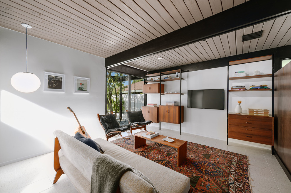 Photo of a mid-sized midcentury enclosed family room in Los Angeles with white walls, a wall-mounted tv and beige floor.