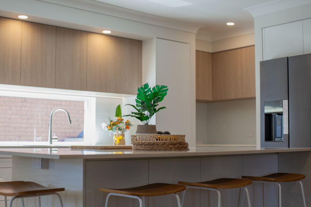Photo of a mid-sized beach style galley eat-in kitchen in Central Coast with an undermount sink, flat-panel cabinets, medium wood cabinets, quartz benchtops, white splashback, subway tile splashback, black appliances, medium hardwood floors, with island, brown floor and grey benchtop.