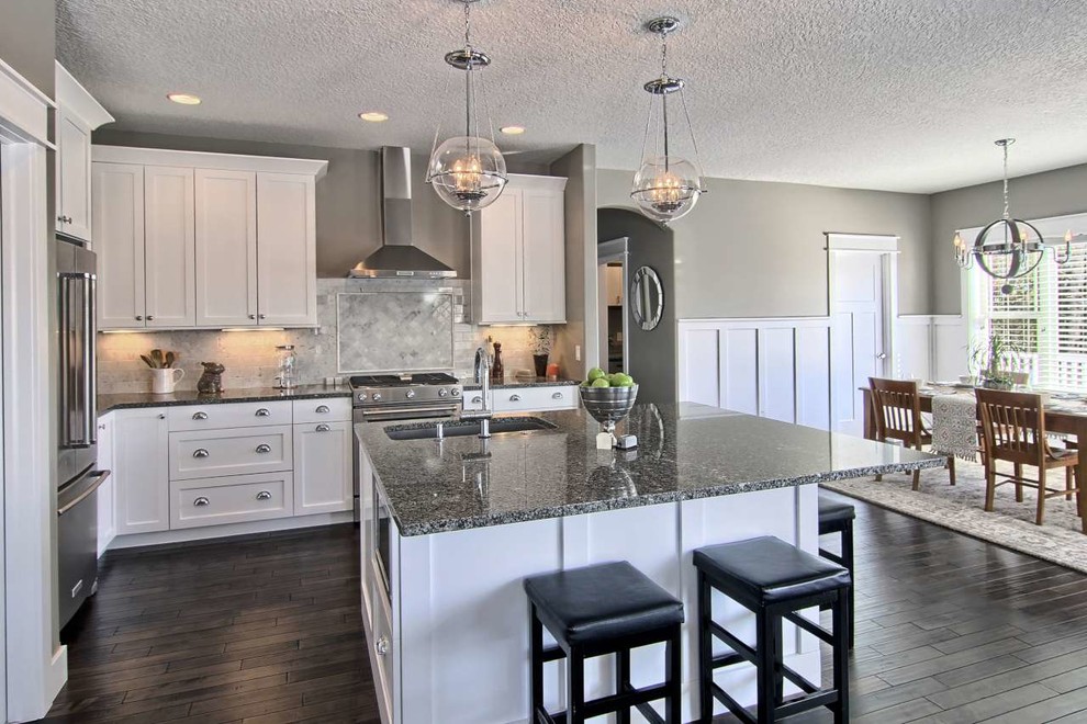 Example of a mid-sized transitional l-shaped dark wood floor open concept kitchen design with a single-bowl sink, shaker cabinets, white cabinets, granite countertops, gray backsplash, stone tile backsplash, stainless steel appliances and an island