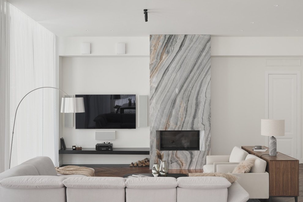 Пример оригинального дизайна: большая открытая, объединенная гостиная комната в белых тонах с отделкой деревом в современном стиле с белыми стенами, паркетным полом среднего тона, стандартным камином, фасадом камина из камня, телевизором на стене и коричневым полом