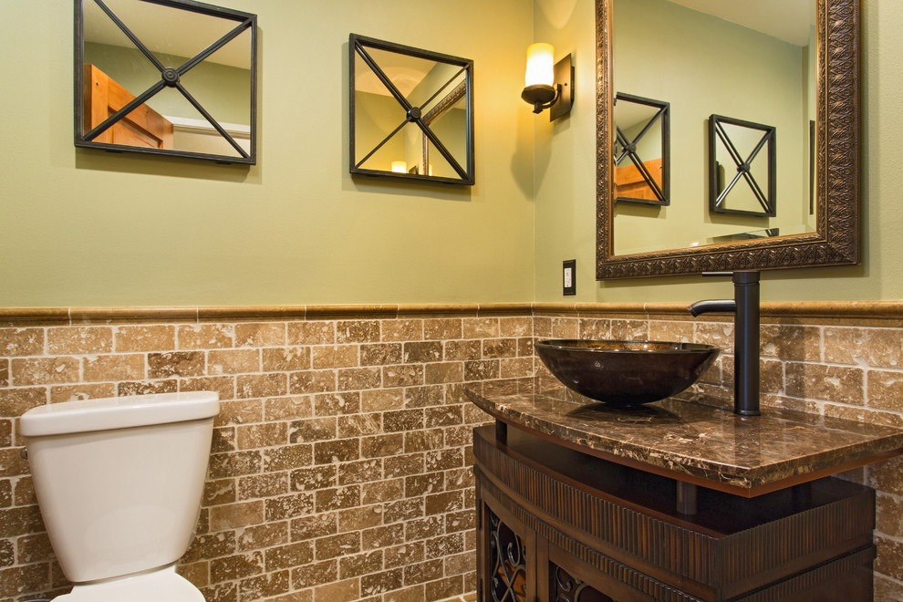 This is an example of a small powder room in Los Angeles with furniture-like cabinets, dark wood cabinets, a two-piece toilet, beige tile, travertine, green walls, travertine floors, a vessel sink, granite benchtops and brown floor.