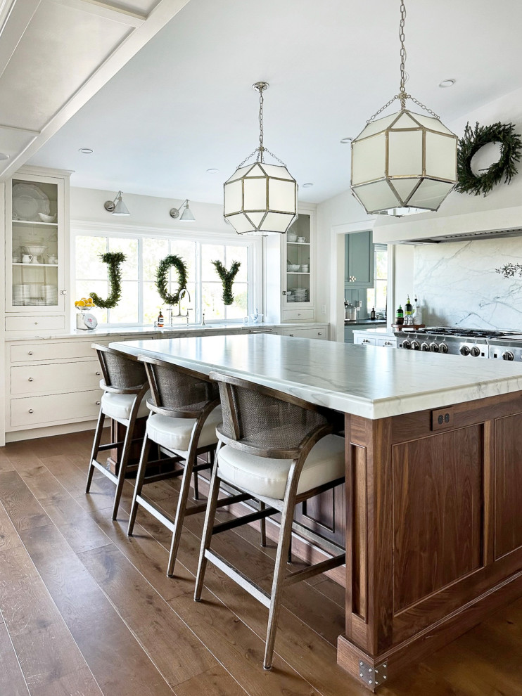 Example of a large transitional u-shaped medium tone wood floor and brown floor eat-in kitchen design with a drop-in sink, shaker cabinets, white cabinets, marble countertops, white backsplash, marble backsplash, stainless steel appliances, an island and white countertops