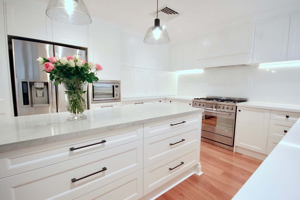 Inspiration for a large transitional u-shaped eat-in kitchen in Sydney with an undermount sink, recessed-panel cabinets, white cabinets, quartz benchtops, white splashback, stone slab splashback, stainless steel appliances, medium hardwood floors, with island, brown floor and white benchtop.