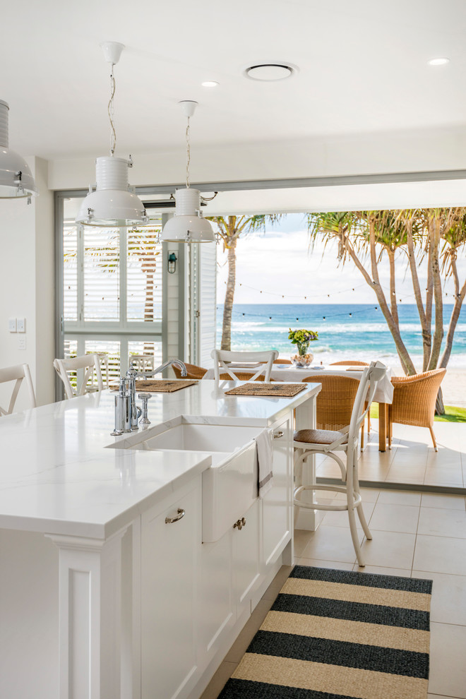 Large beach style galley eat-in kitchen in Gold Coast - Tweed with a farmhouse sink, shaker cabinets, white cabinets, marble benchtops, white splashback, marble splashback, stainless steel appliances, ceramic floors, with island, beige floor and white benchtop.