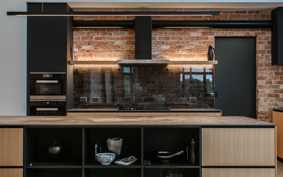 Photo of a large industrial open plan kitchen in Adelaide with a submerged sink, engineered stone countertops, glass sheet splashback, black appliances, concrete flooring, multicoloured worktops and a vaulted ceiling.