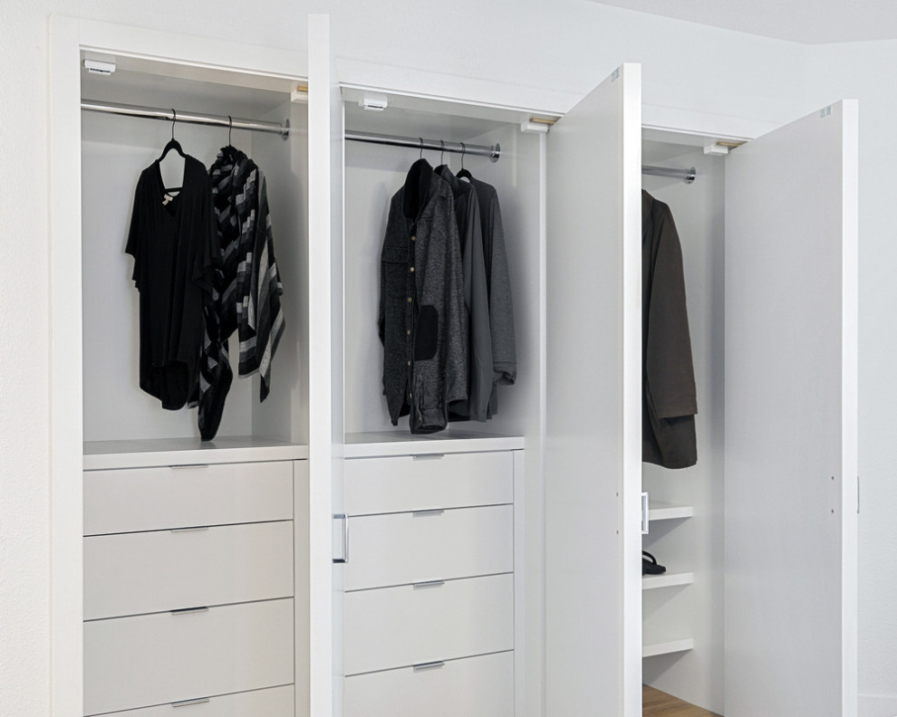 This is an example of a small beach style gender-neutral storage and wardrobe in Orange County with flat-panel cabinets, white cabinets, vinyl floors and brown floor.