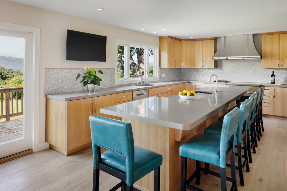 This is an example of a contemporary l-shaped kitchen in San Francisco with a single-bowl sink, flat-panel cabinets, light wood cabinets, grey splashback, stainless steel appliances, light hardwood floors, with island, beige floor and grey benchtop.