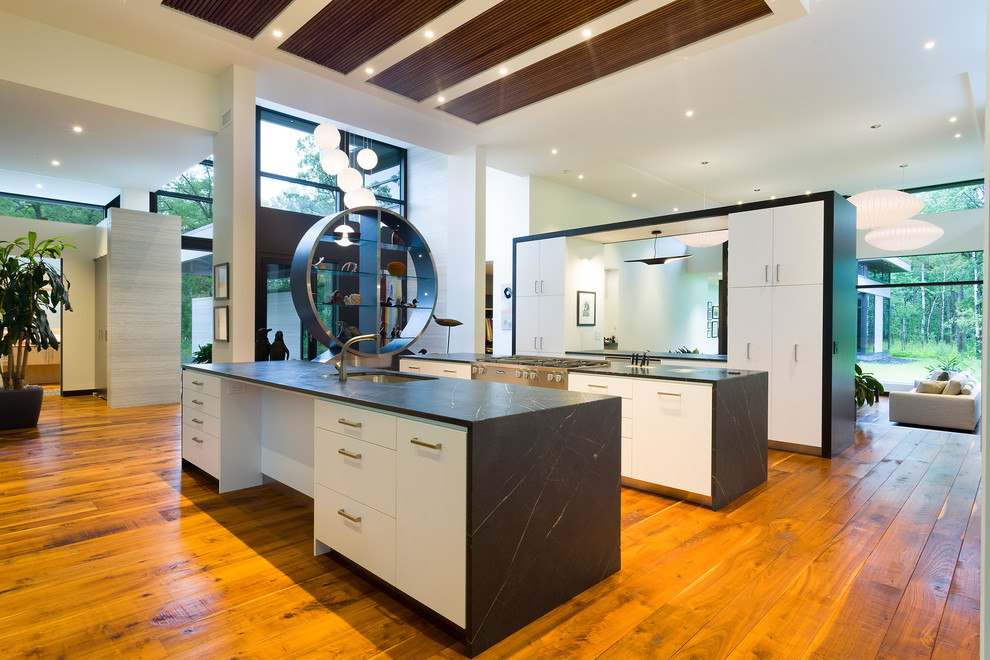 Inspiration for an expansive contemporary galley open plan kitchen in Other with multiple islands, an undermount sink, flat-panel cabinets, white cabinets, soapstone benchtops, white splashback, stainless steel appliances, medium hardwood floors, brown floor and black benchtop.