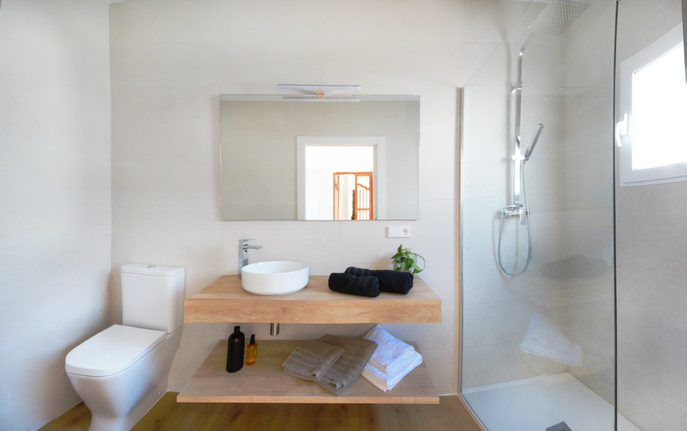This is an example of a mediterranean bathroom in Valencia with open cabinets, medium wood cabinets, a curbless shower, a one-piece toilet, brown tile, wood-look tile, beige walls, wood-look tile, a vessel sink, wood benchtops, brown floor, an open shower, brown benchtops, an enclosed toilet, a single vanity and a floating vanity.