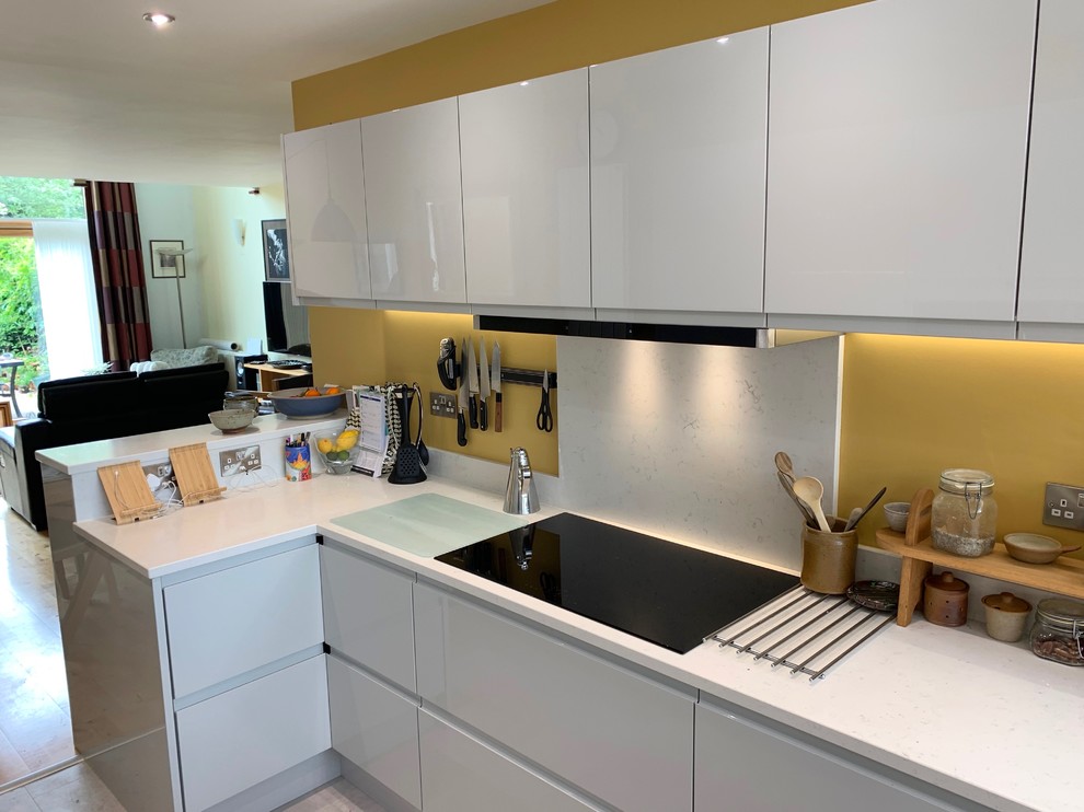 This is an example of a small contemporary u-shaped open plan kitchen in Buckinghamshire with flat-panel cabinets, grey cabinets, quartzite benchtops, white splashback, black appliances, vinyl floors, grey floor and white benchtop.
