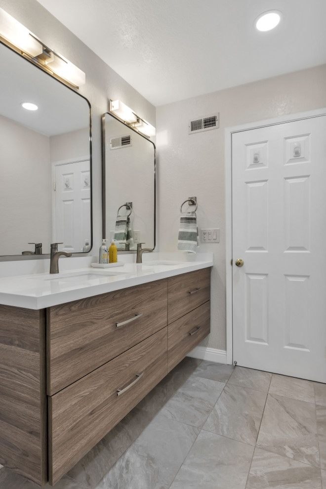 This is an example of a small modern 3/4 bathroom in Phoenix with flat-panel cabinets, brown cabinets, an alcove shower, a two-piece toilet, ceramic tile, grey walls, ceramic floors, engineered quartz benchtops, grey floor, a hinged shower door, white benchtops, a double vanity, a floating vanity, brick walls and gray tile.