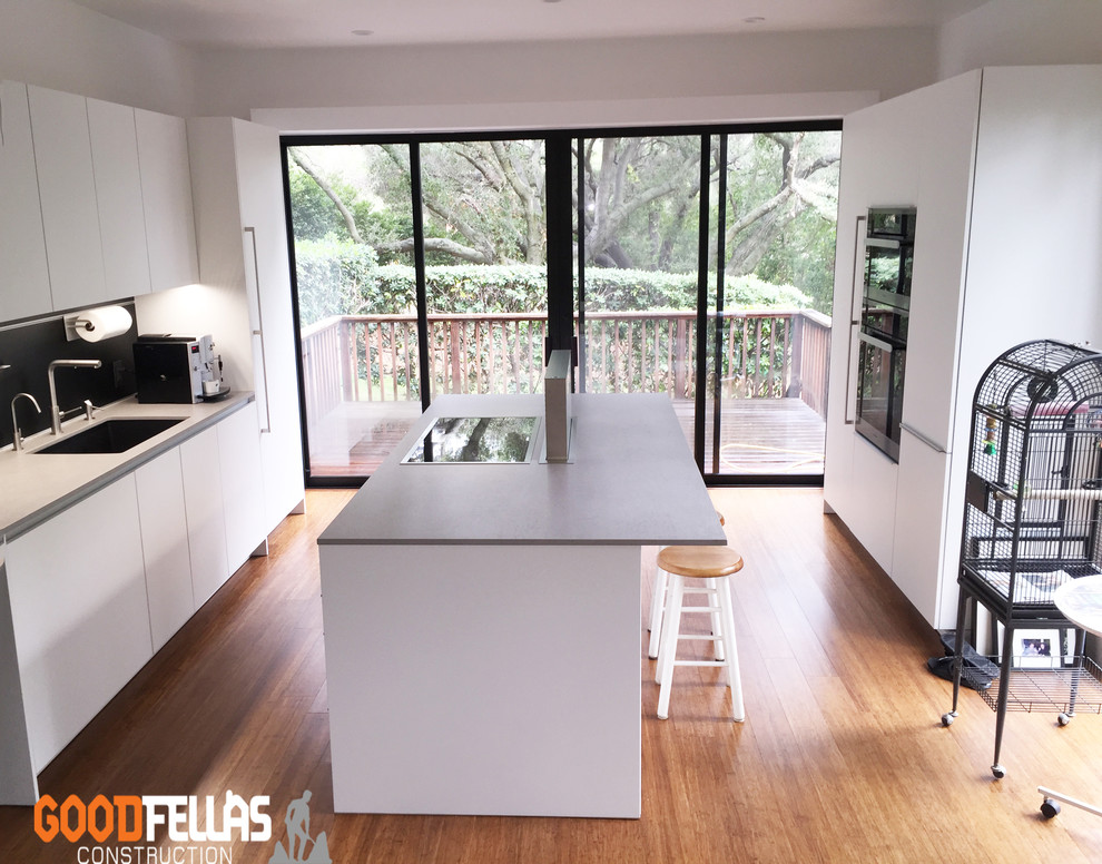 Design ideas for a mid-sized tropical l-shaped eat-in kitchen in San Francisco with an integrated sink, flat-panel cabinets, white cabinets, limestone benchtops, black splashback, ceramic splashback, stainless steel appliances, light hardwood floors and a peninsula.