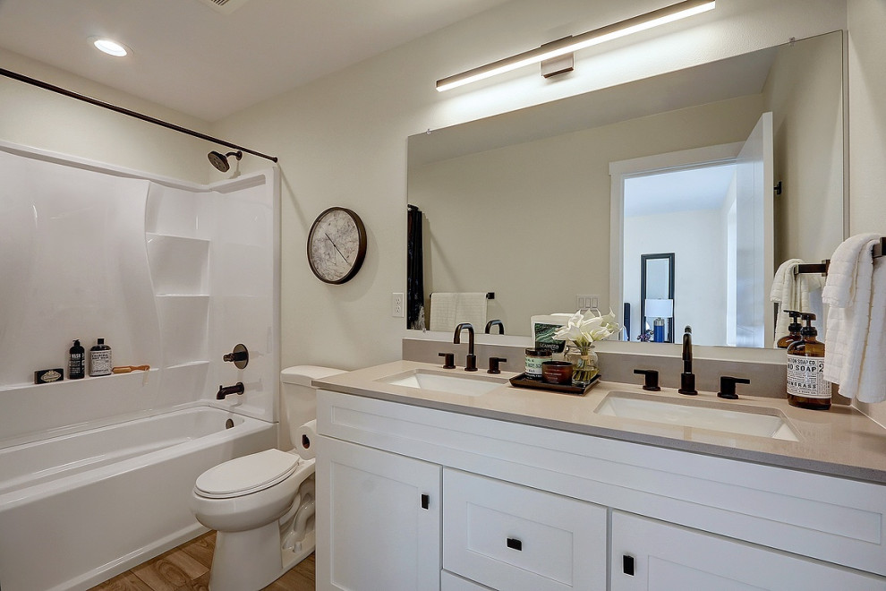 Inredning av ett klassiskt litet grå grått en-suite badrum, med skåp i shakerstil, vita skåp, ett badkar i en alkov, en toalettstol med separat cisternkåpa, grå väggar, laminatgolv, ett undermonterad handfat, bänkskiva i kvarts, brunt golv och dusch med duschdraperi