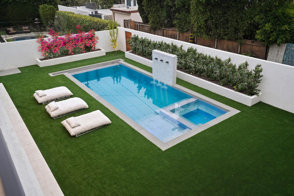 This is an example of a large modern back rectangular swimming pool with a water feature and tiled flooring.