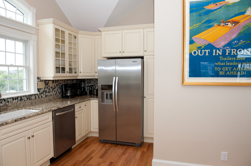 Large transitional light wood floor open concept kitchen photo with an undermount sink, raised-panel cabinets, beige cabinets, granite countertops, multicolored backsplash, mosaic tile backsplash, stainless steel appliances and a peninsula