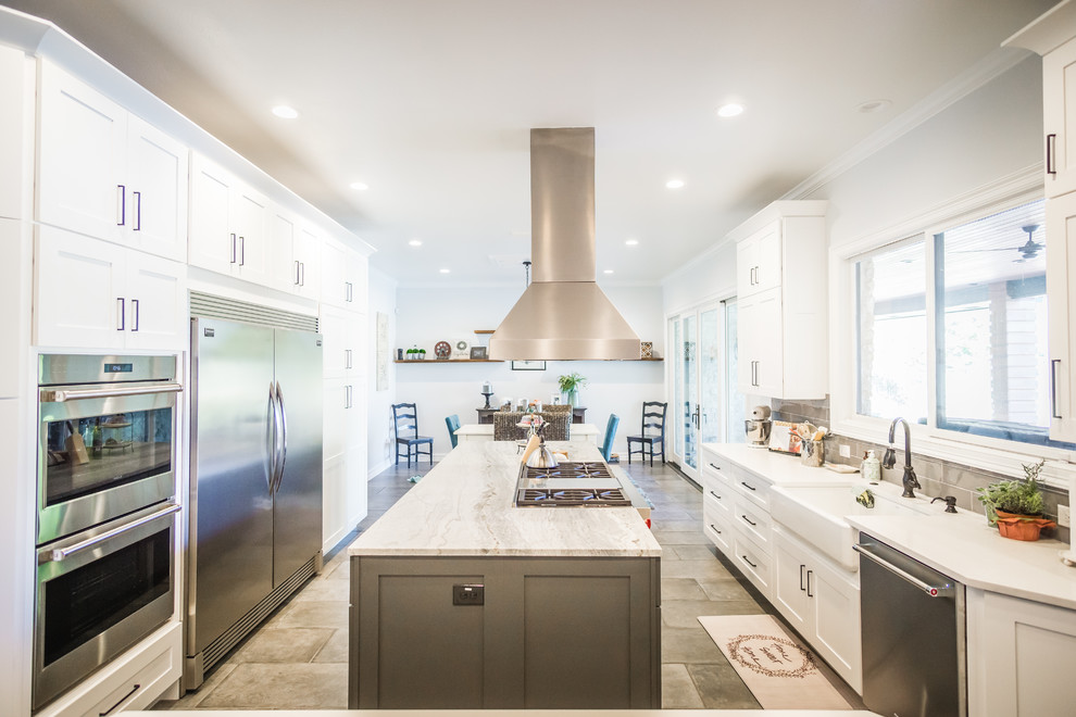 This is an example of a large country galley eat-in kitchen in Austin with a farmhouse sink, shaker cabinets, white cabinets, granite benchtops, grey splashback, glass tile splashback, stainless steel appliances, cement tiles, multiple islands and grey floor.