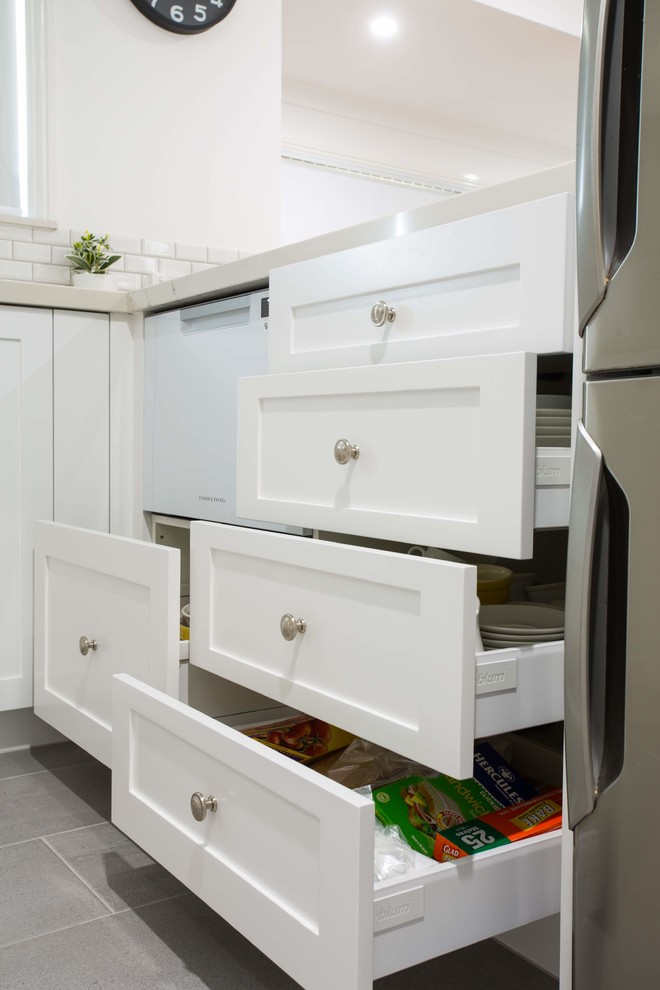 Photo of a small traditional u-shaped kitchen pantry in Brisbane with a double-bowl sink, shaker cabinets, white cabinets, quartz benchtops, grey splashback, ceramic splashback, black appliances, porcelain floors, with island, grey floor and white benchtop.