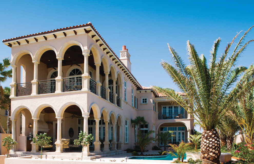 This is an example of a large traditional two-storey stucco beige house exterior in Miami with a hip roof and a tile roof.