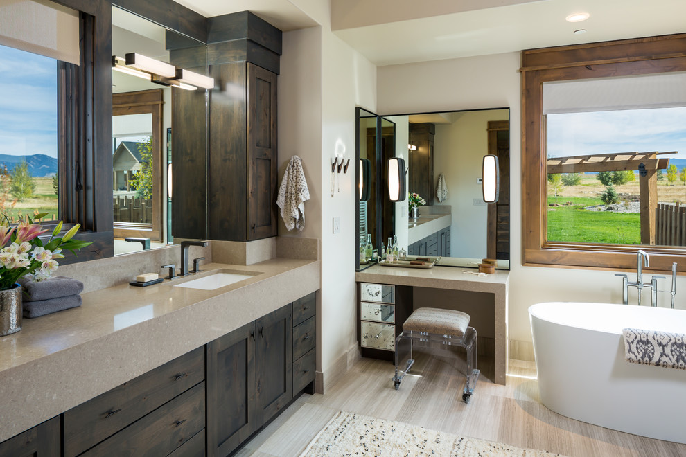 Large mountain style limestone floor and beige floor freestanding bathtub photo with shaker cabinets, white walls, an undermount sink, quartz countertops and dark wood cabinets