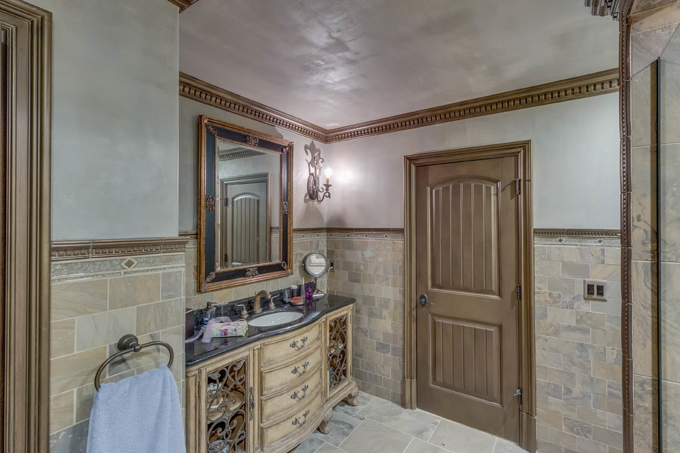 Photo of a mid-sized traditional 3/4 bathroom in Detroit with furniture-like cabinets, distressed cabinets, marble benchtops, an alcove shower, grey walls, ceramic floors, an undermount sink, beige floor, a hinged shower door, beige tile, brown tile, ceramic tile and a two-piece toilet.