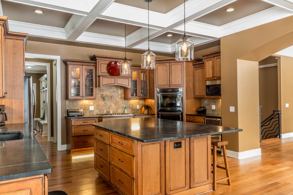 This is an example of a large arts and crafts u-shaped eat-in kitchen in Detroit with an undermount sink, flat-panel cabinets, light wood cabinets, soapstone benchtops, green splashback, slate splashback, black appliances, medium hardwood floors and with island.