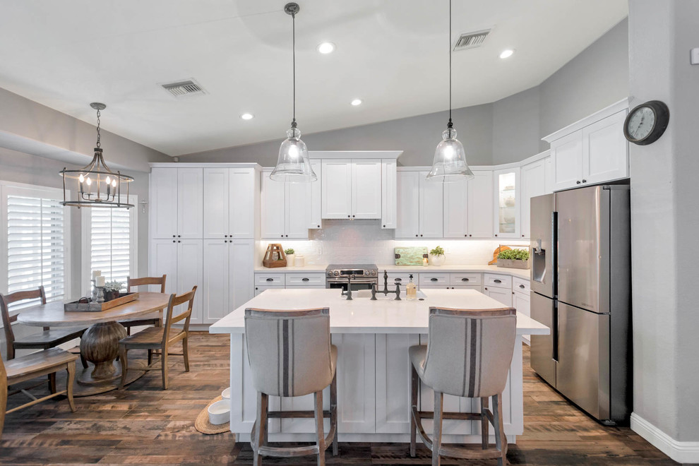 Design ideas for a large country l-shaped open plan kitchen in Phoenix with a farmhouse sink, shaker cabinets, white cabinets, quartz benchtops, white splashback, subway tile splashback, stainless steel appliances, with island and white benchtop.
