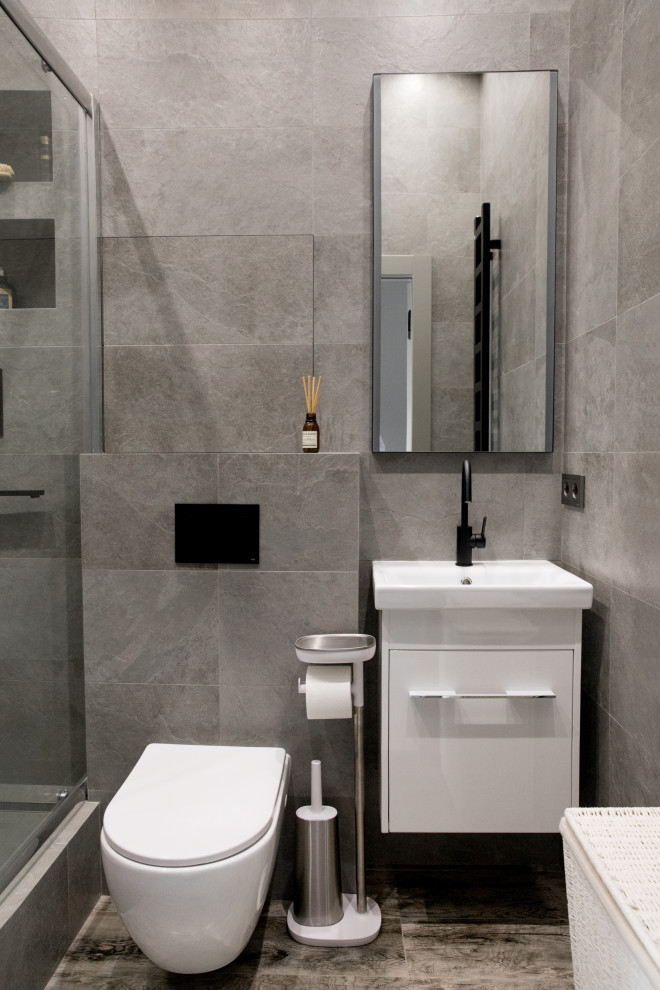 Стильный дизайн: серо-белая ванная комната среднего размера в скандинавском стиле с плоскими фасадами, белыми фасадами, душем в нише, инсталляцией, серой плиткой, керамогранитной плиткой, серыми стенами, полом из керамогранита, душевой кабиной, серым полом, душем с раздвижными дверями, зеркалом с подсветкой, тумбой под одну раковину и подвесной тумбой - последний тренд