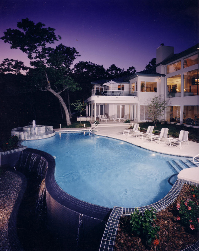 Photo of a large modern backyard custom-shaped infinity pool in Other with a water feature and tile.
