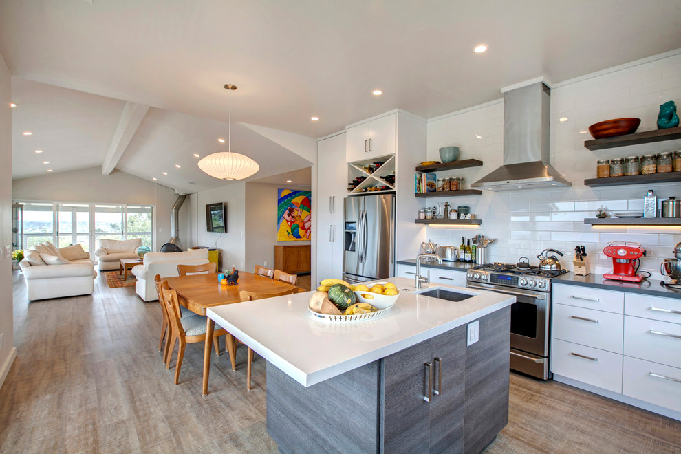Large eclectic l-shaped open plan kitchen in San Diego with a single-bowl sink, flat-panel cabinets, white cabinets, quartz benchtops, white splashback, subway tile splashback, stainless steel appliances, light hardwood floors and with island.