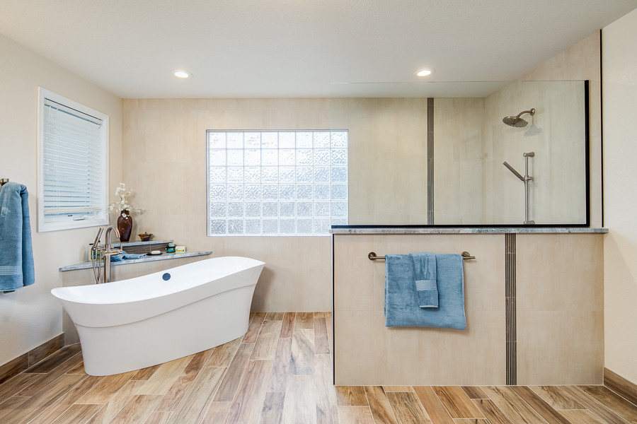 This is an example of an expansive traditional master bathroom in Denver with raised-panel cabinets, medium wood cabinets, a freestanding tub, a curbless shower, a one-piece toilet, beige tile, brown tile, porcelain tile, beige walls, porcelain floors, an undermount sink, granite benchtops, brown floor and an open shower.