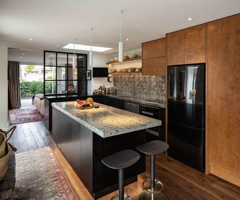 Small contemporary l-shaped eat-in kitchen in Auckland with an undermount sink, flat-panel cabinets, black cabinets, terrazzo benchtops, grey splashback, mosaic tile splashback, black appliances, dark hardwood floors, with island, brown floor and grey benchtop.