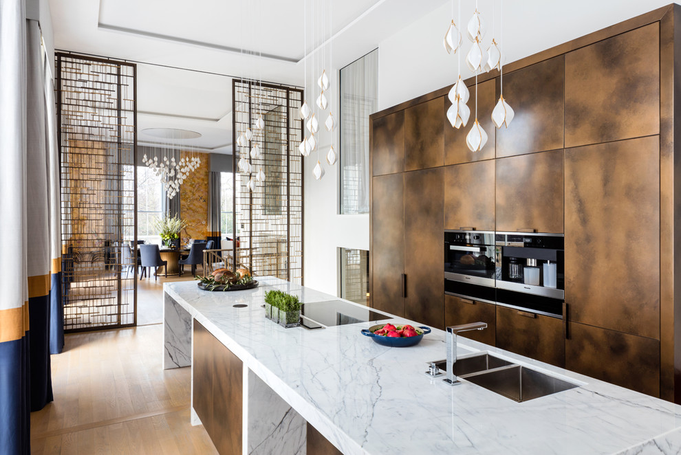 Inspiration for a contemporary galley separate kitchen in London with a double-bowl sink, flat-panel cabinets, brown cabinets, marble benchtops, black appliances, light hardwood floors, with island and beige floor.