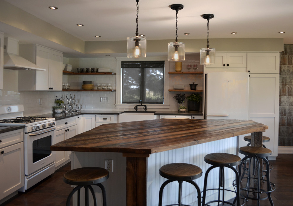 Large industrial l-shaped eat-in kitchen in Chicago with a farmhouse sink, shaker cabinets, white cabinets, wood benchtops, white splashback, subway tile splashback, white appliances, medium hardwood floors, with island and brown floor.