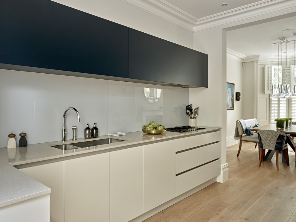 Inspiration for a large contemporary galley eat-in kitchen in London with an undermount sink, flat-panel cabinets, blue cabinets, quartz benchtops, grey splashback, glass sheet splashback, stainless steel appliances and light hardwood floors.