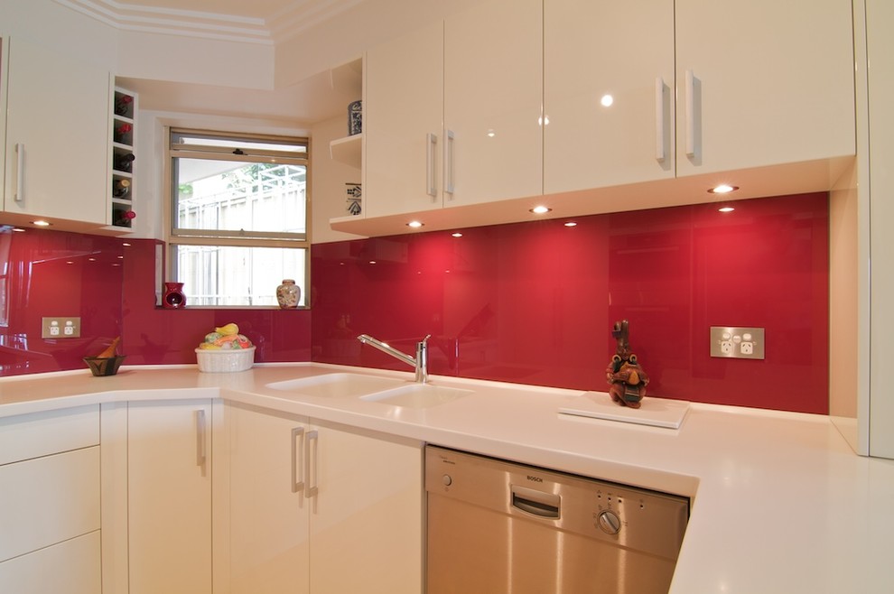 Inspiration for a small modern u-shaped separate kitchen in Sydney with an integrated sink, flat-panel cabinets, white cabinets, solid surface benchtops, red splashback, glass sheet splashback, stainless steel appliances, light hardwood floors and no island.