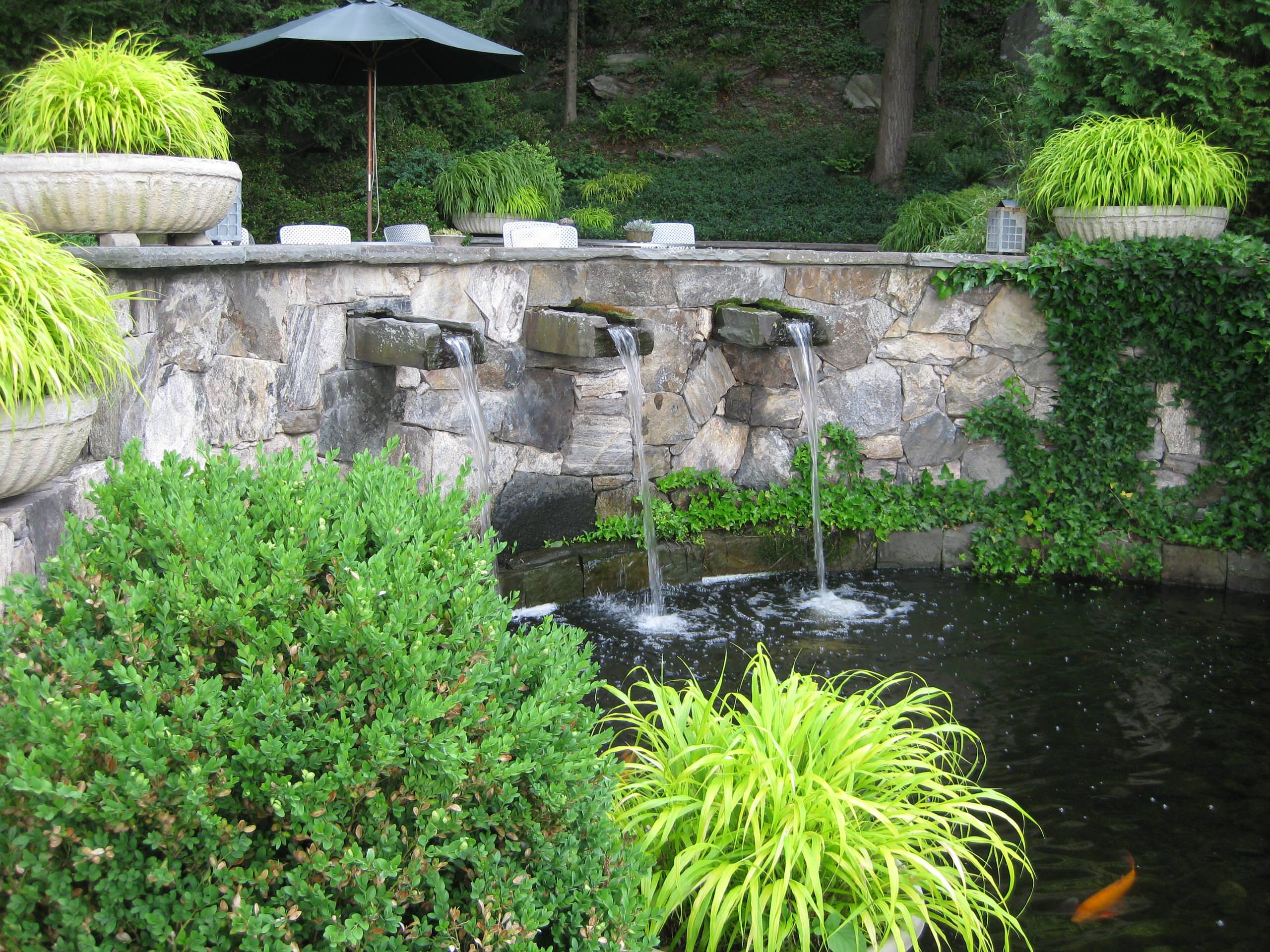 KOI POND WITH PATIO ABOVE. HAKENCLAWA GRASSES FILL THE POTS AT THE TERRACE. PETER ATKINS AND ASSOCIATES, LLC