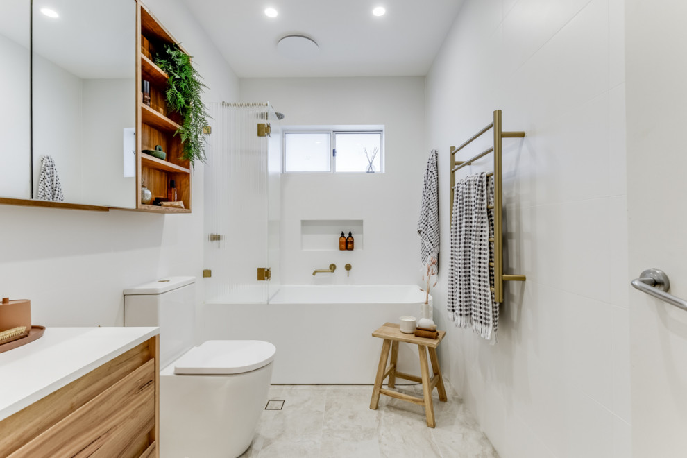 Small modern family bathroom in Sydney with flat-panel cabinets, light wood cabinets, a corner bath, a shower/bath combination, a two-piece toilet, white tiles, white walls, a vessel sink, grey floors, a hinged door, white worktops, a wall niche, a single sink and a floating vanity unit.