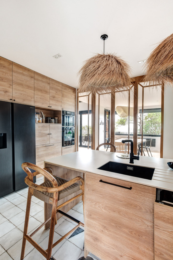 This is an example of a small beach style l-shaped kitchen in Other with an integrated sink, medium wood cabinets, stone tile splashback, black appliances, with island and white benchtop.