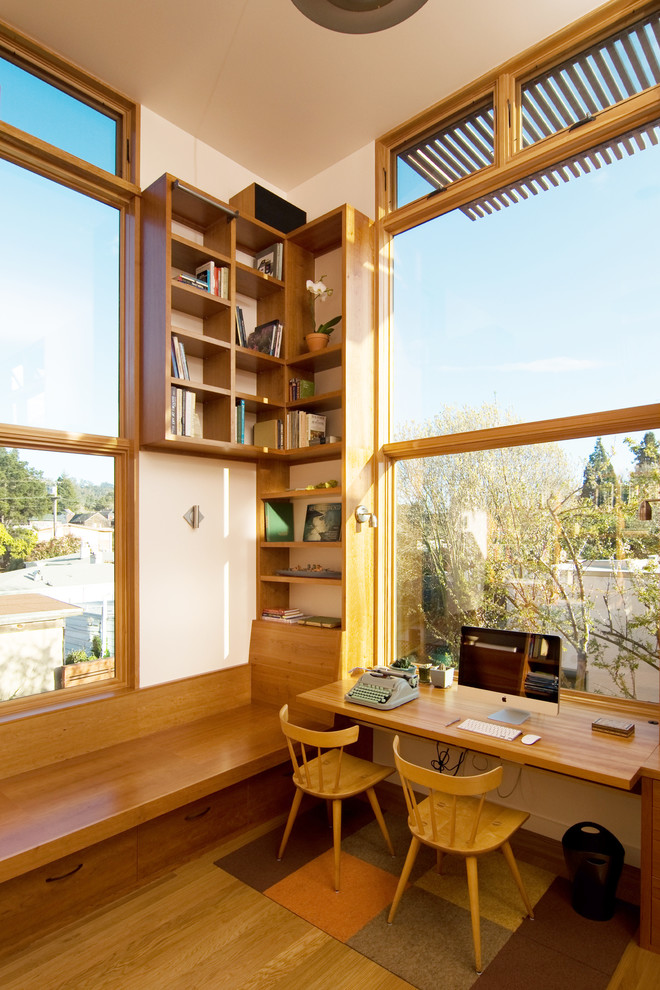 This is an example of a mid-sized contemporary home office in San Francisco with white walls, medium hardwood floors, a built-in desk and no fireplace.