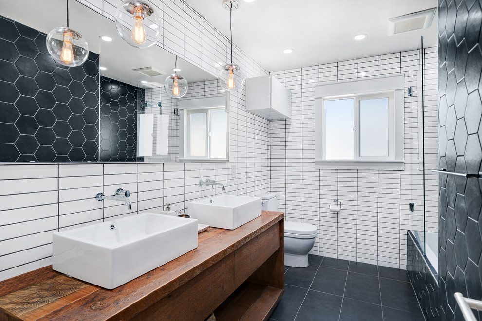 Photo of a midcentury master bathroom in San Francisco with flat-panel cabinets, dark wood cabinets, a drop-in tub, a shower/bathtub combo, black tile, black and white tile, white tile, matchstick tile, white walls, a vessel sink, wood benchtops, black floor, an open shower and brown benchtops.