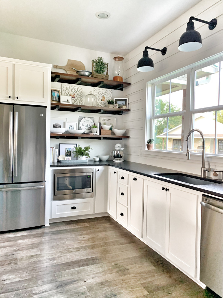 Large country u-shaped eat-in kitchen with an undermount sink, shaker cabinets, white cabinets, granite benchtops, white splashback, shiplap splashback, stainless steel appliances, vinyl floors, with island, grey floor and black benchtop.