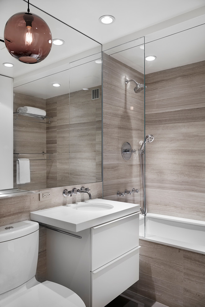 Photo of a large contemporary master bathroom in New York with flat-panel cabinets, an undermount sink, grey walls, a drop-in tub, a shower/bathtub combo, brown tile, gray tile, travertine floors, engineered quartz benchtops, a two-piece toilet, limestone, white benchtops and white cabinets.