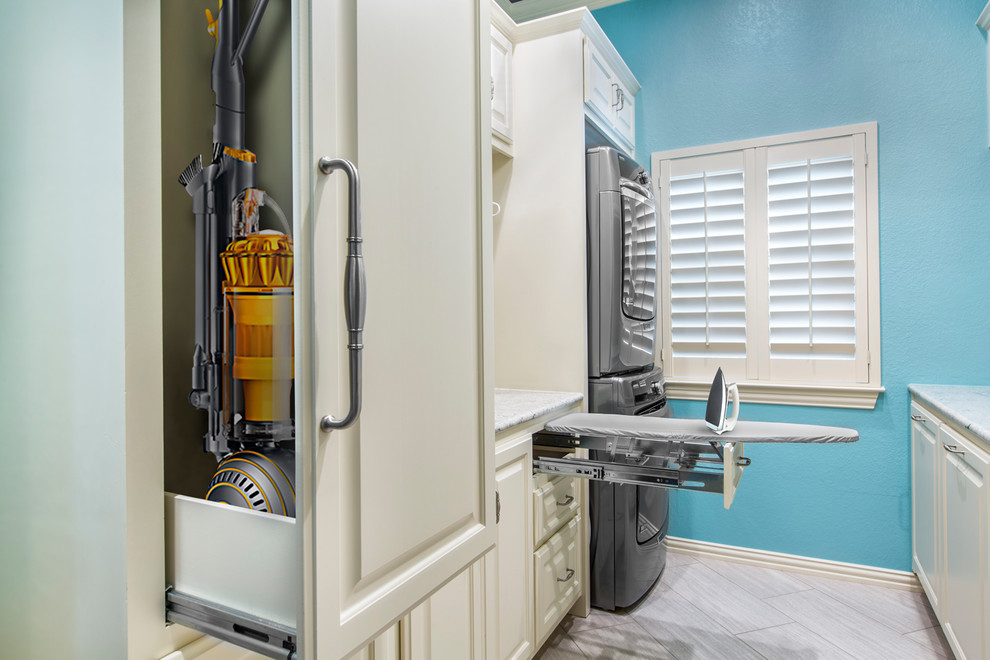 Inspiration for a large modern galley dedicated laundry room in Other with an undermount sink, raised-panel cabinets, white cabinets, granite benchtops, blue walls, ceramic floors, a stacked washer and dryer and beige floor.