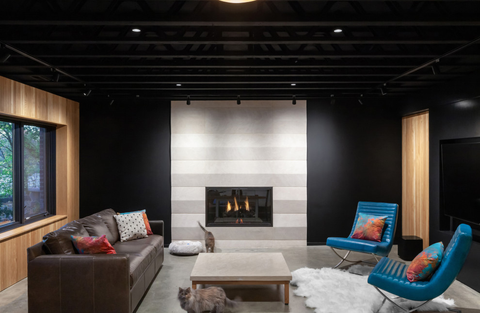 This is an example of a mid-sized scandinavian walk-out basement in Indianapolis with black walls, concrete floors, a standard fireplace, a stone fireplace surround, grey floor, exposed beam and wood walls.