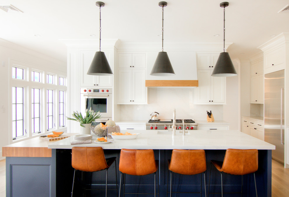 Large transitional l-shaped eat-in kitchen in New York with a farmhouse sink, flat-panel cabinets, white cabinets, quartzite benchtops, white splashback, stone slab splashback, stainless steel appliances, light hardwood floors, multiple islands, yellow floor and white benchtop.