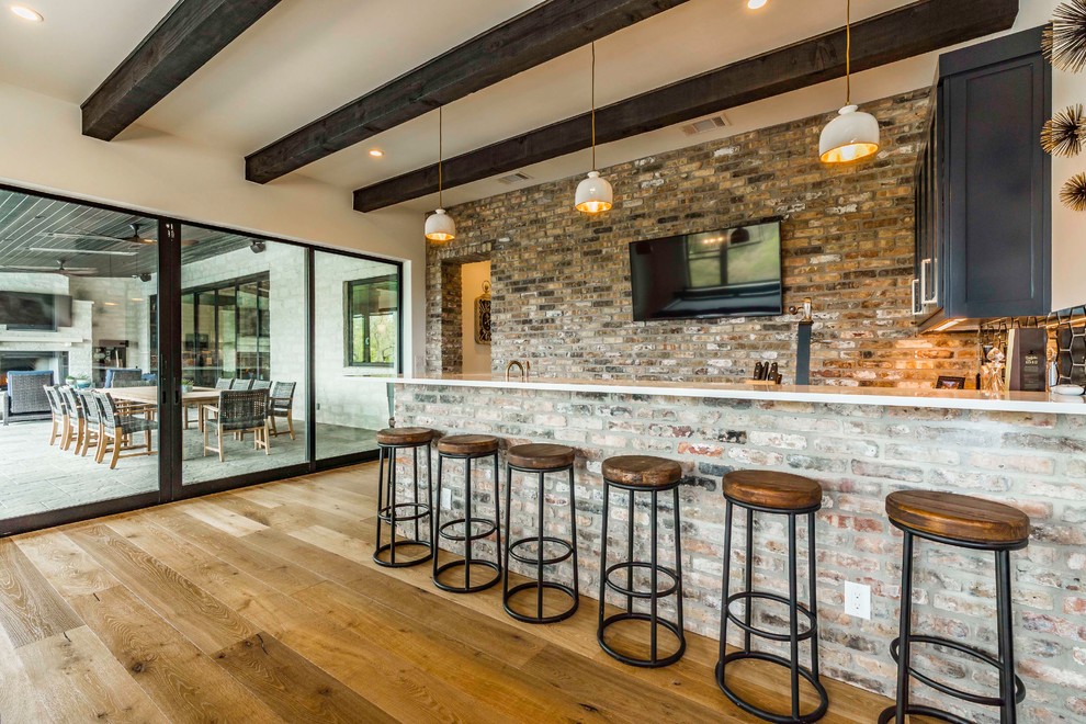 Country seated home bar in Austin with dark wood cabinets, brick splashback and medium hardwood floors.