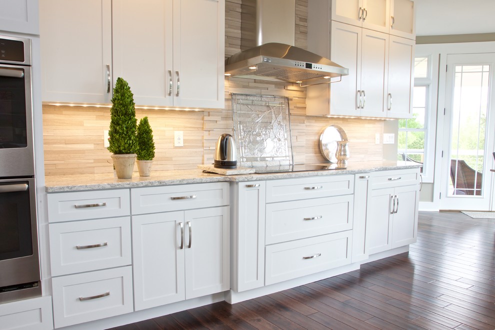 Eat-in kitchen - mid-sized transitional galley eat-in kitchen idea with white cabinets, granite countertops, beige backsplash, stone tile backsplash and stainless steel appliances